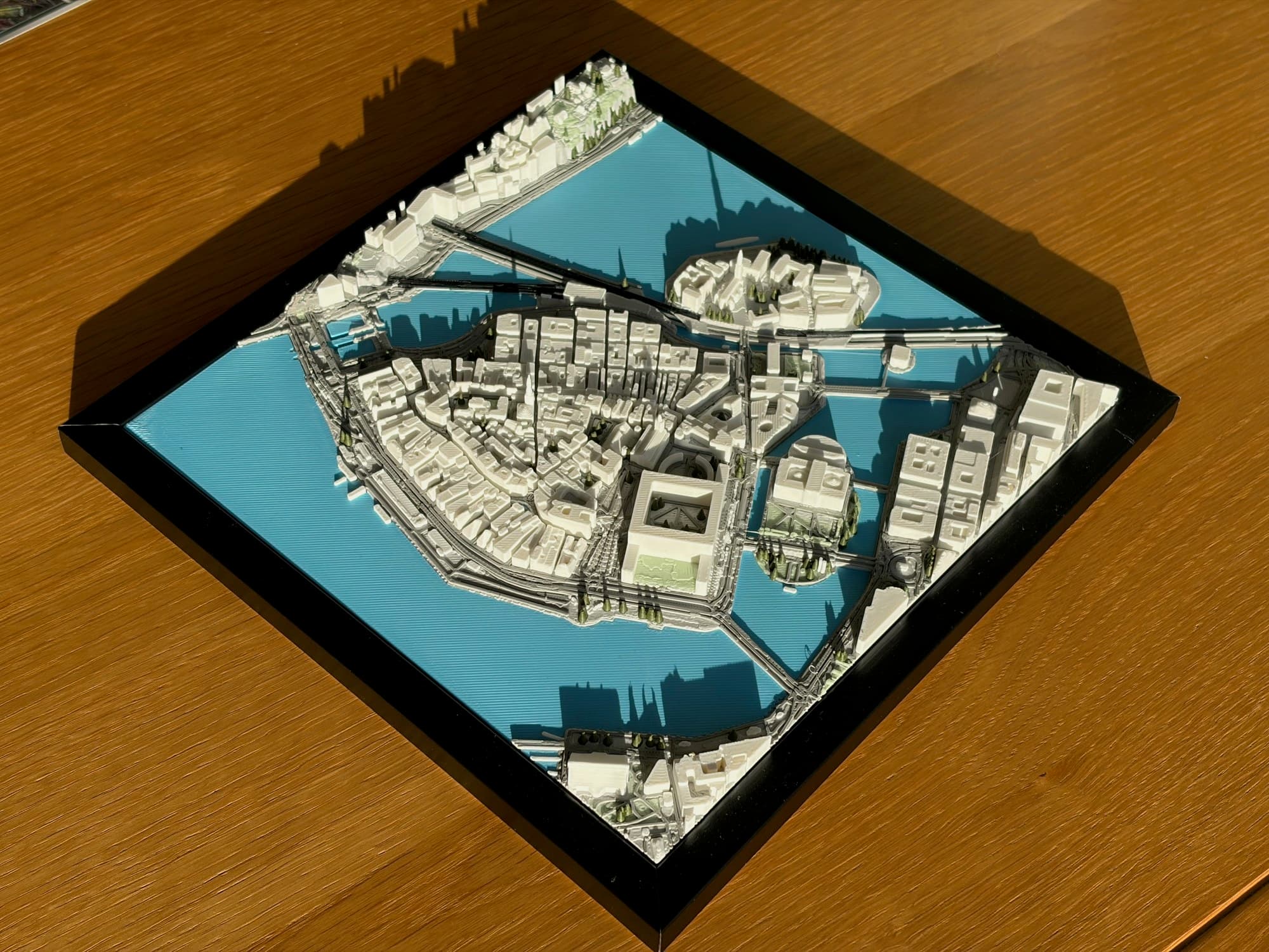 Black-framed 3D city map of Gamla Stan in sunlight on an oak table.